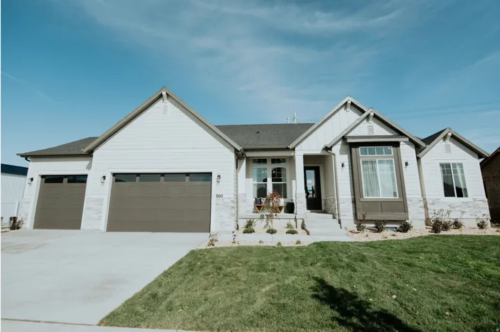 Modern farmhouse style home featuring an attached garage, driveway, board and batten siding, a front yard, and stone siding