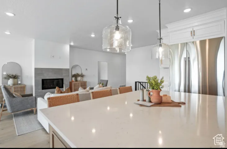 Kitchen with light hardwood / wood-style floors, stainless steel fridge, pendant lighting, a fireplace, and white cabinets