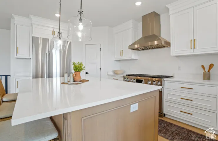 Kitchen featuring white cabinets, stainless steel appliances, wall chimney exhaust hood, and a spacious island