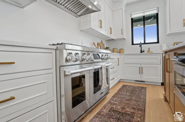 Kitchen with white cabinets, double oven range, light wood-type flooring, and sink