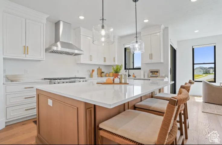 Kitchen featuring white cabinets, a center island, light hardwood / wood-style flooring, hanging light fixtures, and wall chimney range hood