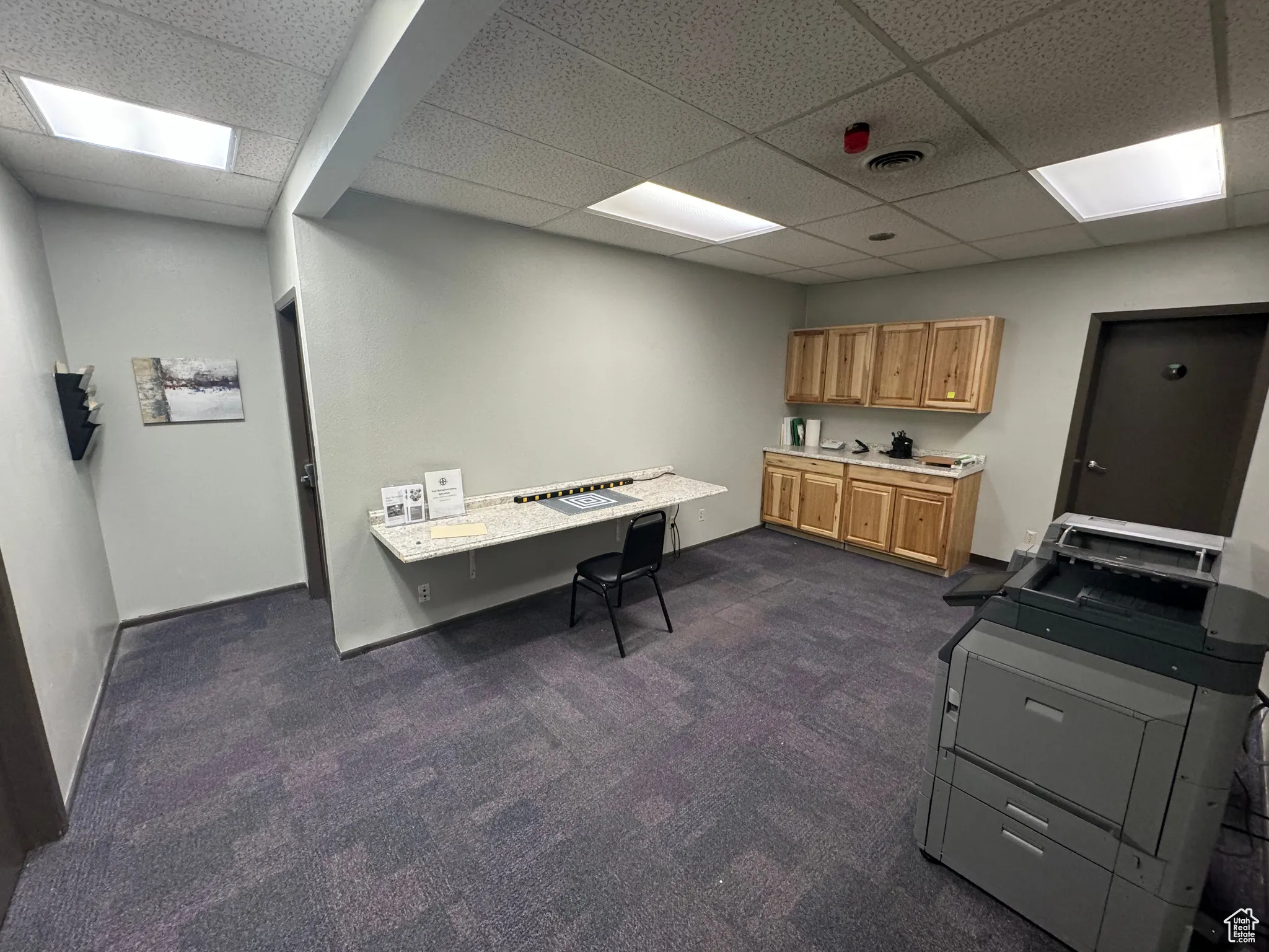 Home office with a paneled ceiling and dark colored carpet