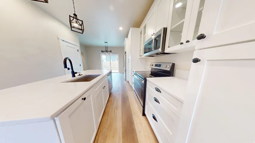 Kitchen with stainless steel appliances, white cabinets, light wood-type flooring, hanging light fixtures, and a center island with sink