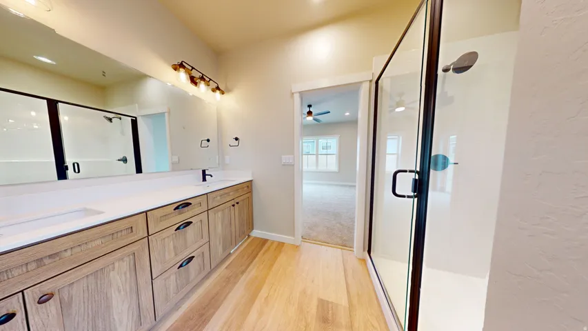 Bathroom with a stall shower, double vanity, light wood-style floors, and a textured wall