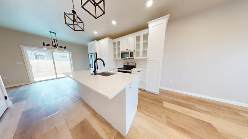 Kitchen featuring decorative light fixtures, glass insert cabinets, an island with sink, recessed lighting, and stainless steel appliances