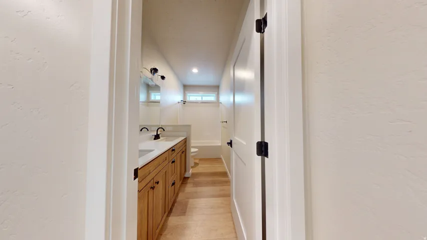 Full bathroom with a textured wall, double vanity, and light wood finished floors