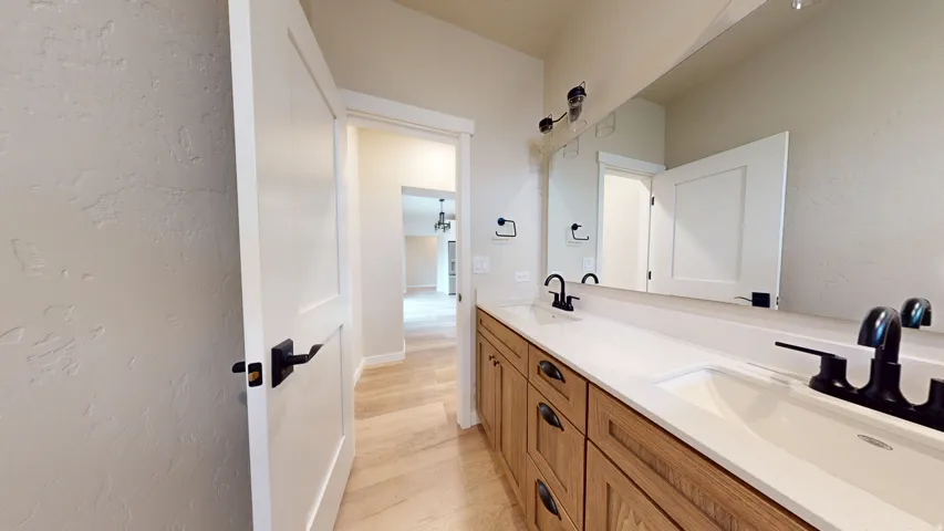 Full bathroom with a textured wall, double vanity, and light wood-style floors