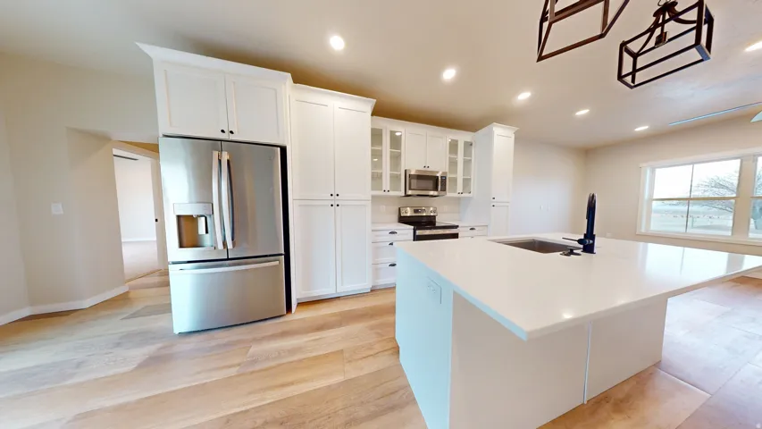 Kitchen featuring glass insert cabinets, stainless steel appliances, white cabinetry, recessed lighting, and an island with sink