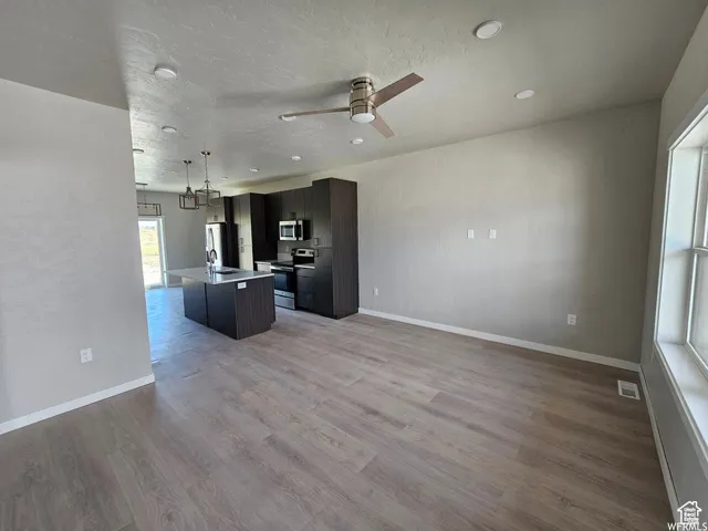 Kitchen with ceiling fan, light hardwood / wood-style flooring, pendant lighting, a kitchen island with sink, and appliances with stainless steel finishes