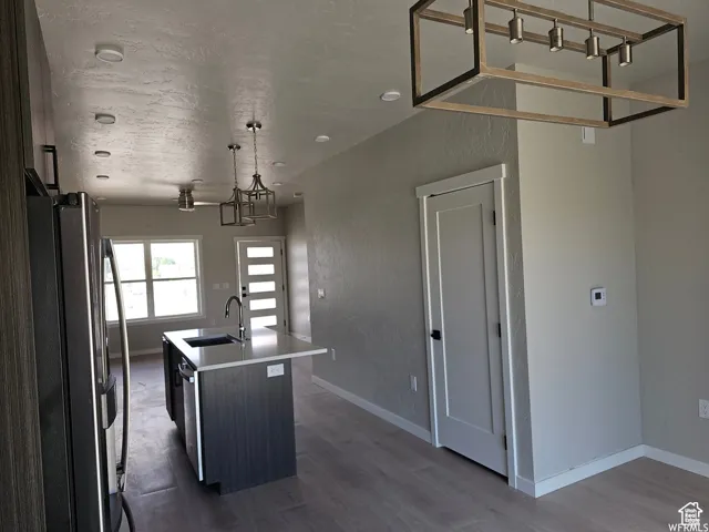 Kitchen with a center island with sink, sink, appliances with stainless steel finishes, wood-type flooring, and a chandelier
