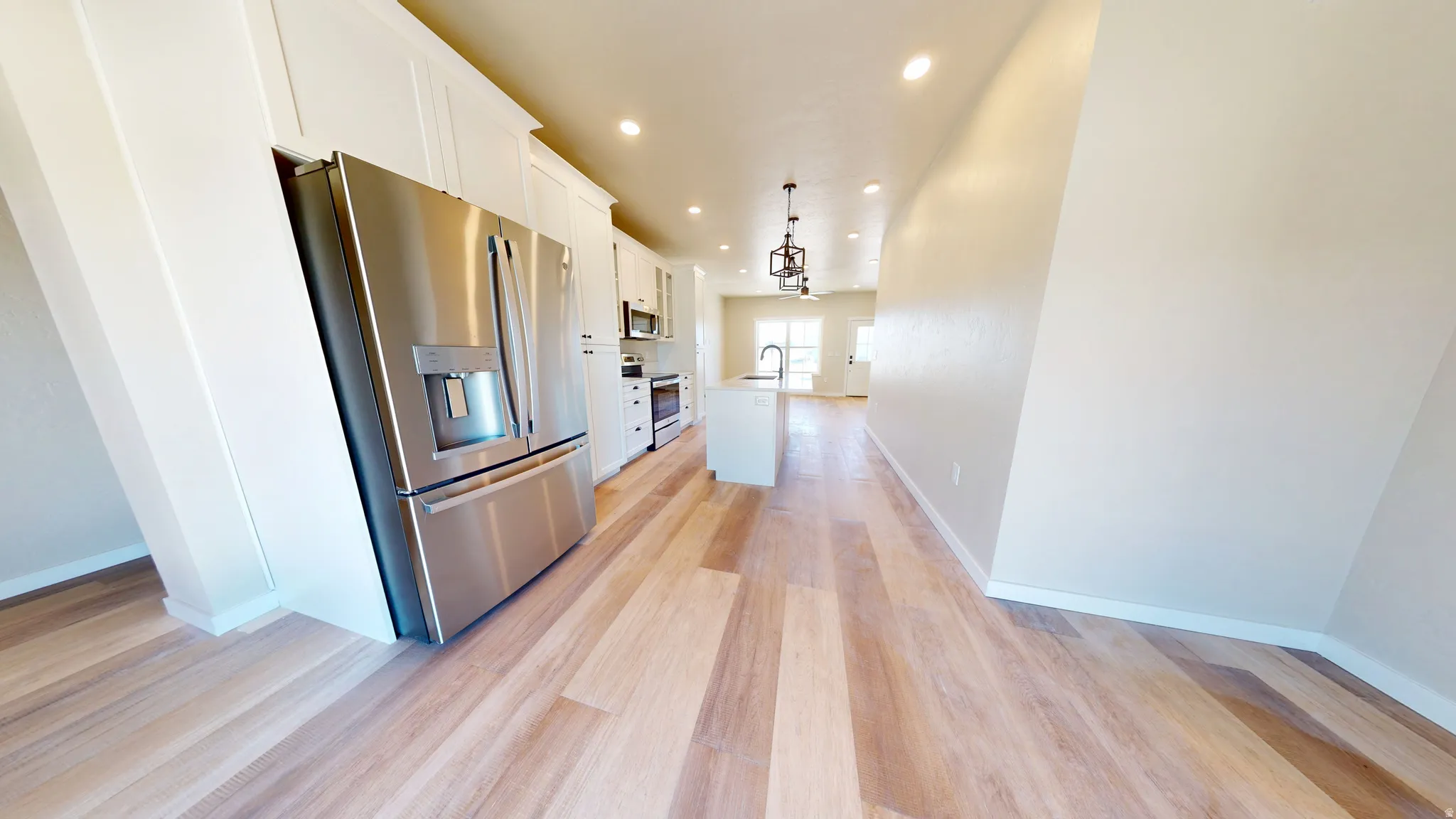 Kitchen featuring appliances with stainless steel finishes, white cabinetry, recessed lighting, light wood finished floors, and decorative light fixtures
