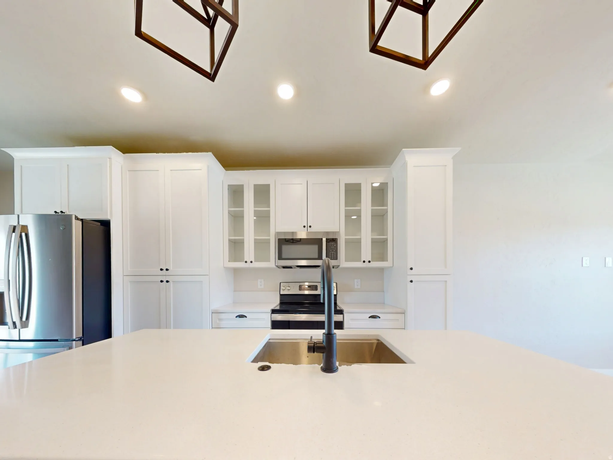 Kitchen with glass insert cabinets, recessed lighting, appliances with stainless steel finishes, white cabinets, and a kitchen island with sink