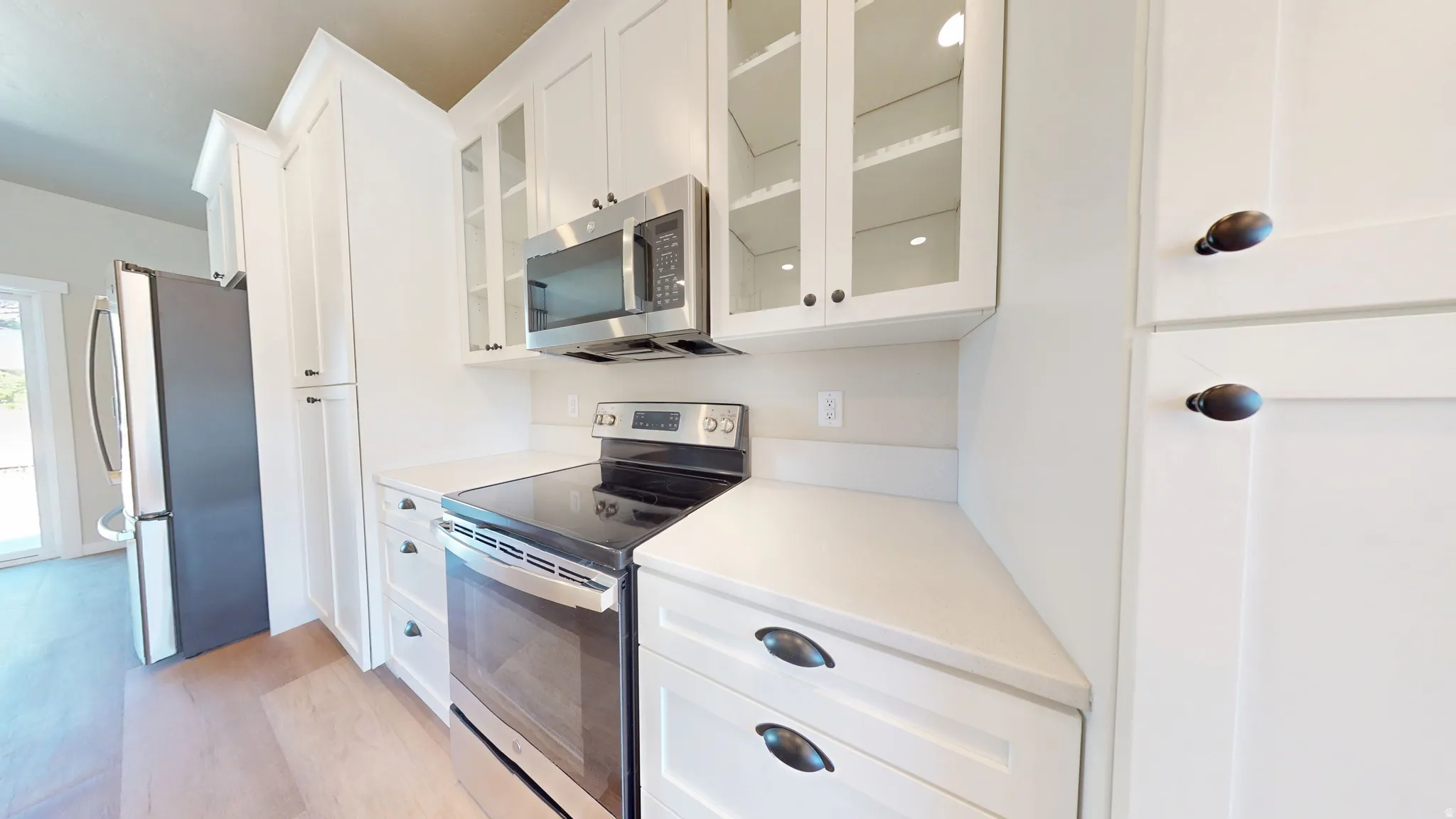 Kitchen featuring stainless steel appliances, white cabinets, glass insert cabinets, and light wood finished floors