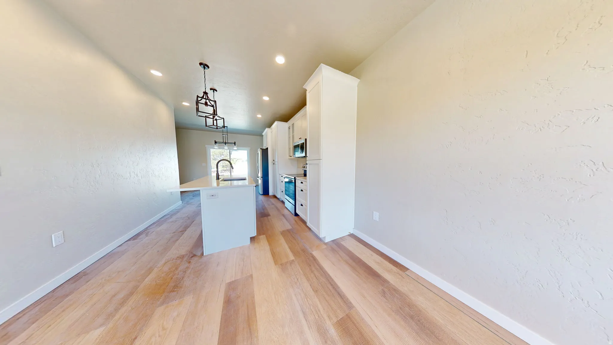 Kitchen with a kitchen island with sink, white cabinetry, light wood finished floors, a textured wall, and decorative light fixtures