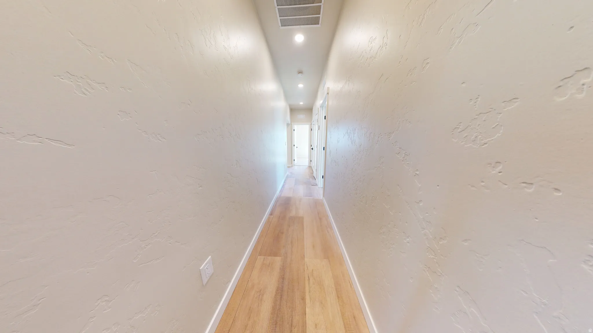 Hall featuring a textured wall, light wood-style floors, and recessed lighting