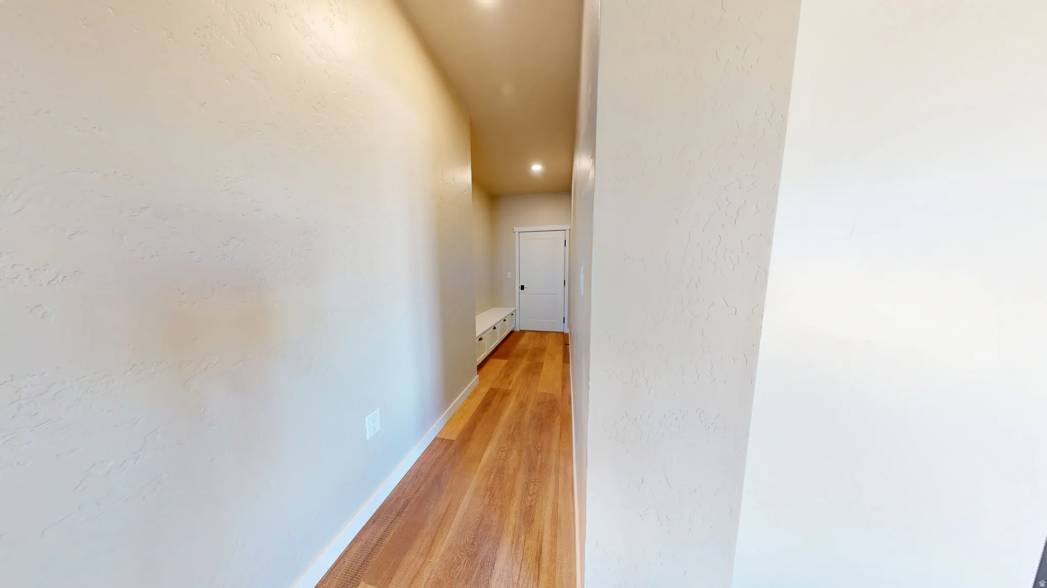 Hallway featuring light wood finished floors and a textured wall