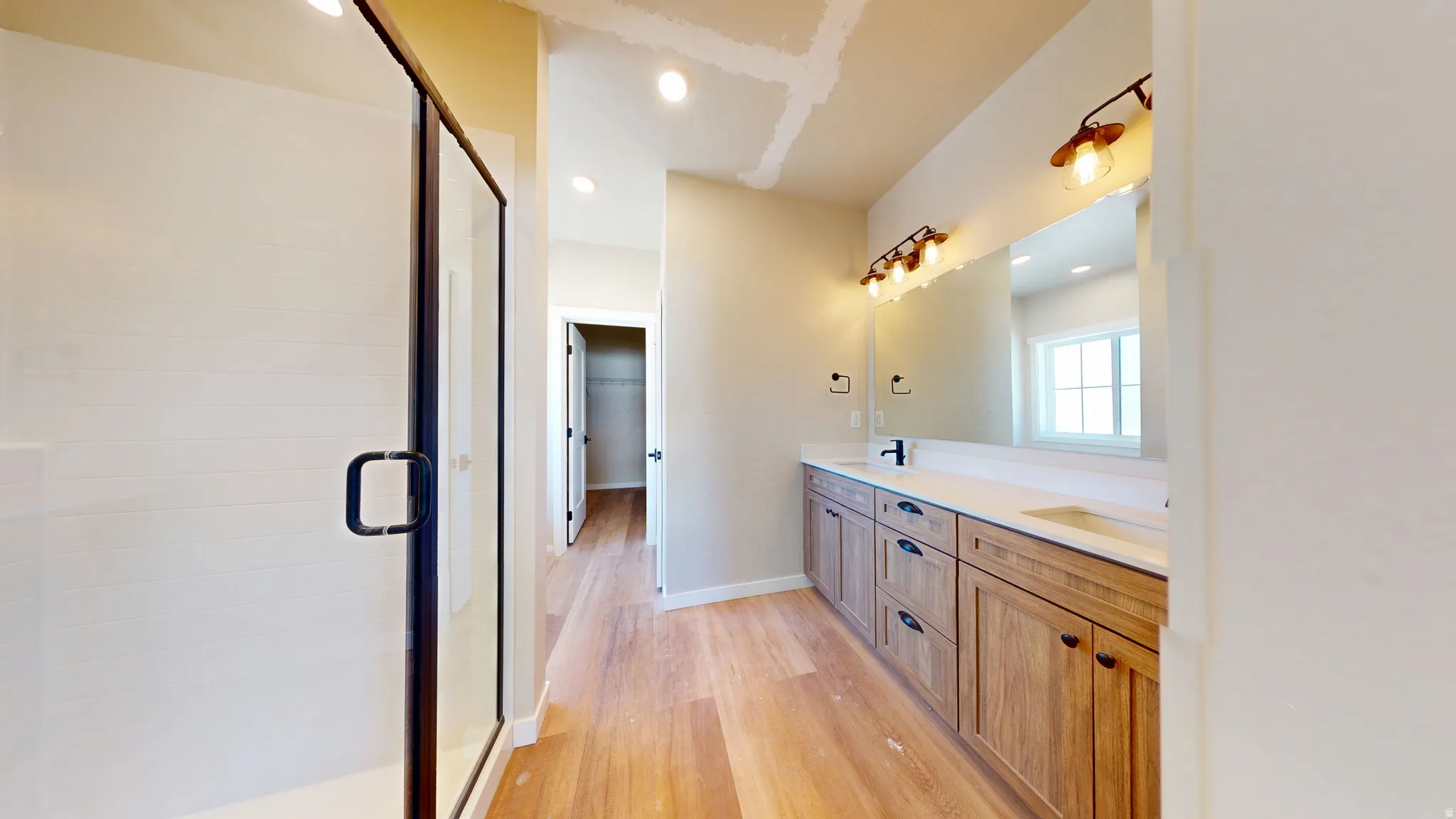 Bathroom with double vanity, light wood-type flooring, recessed lighting, a stall shower, and a walk in closet