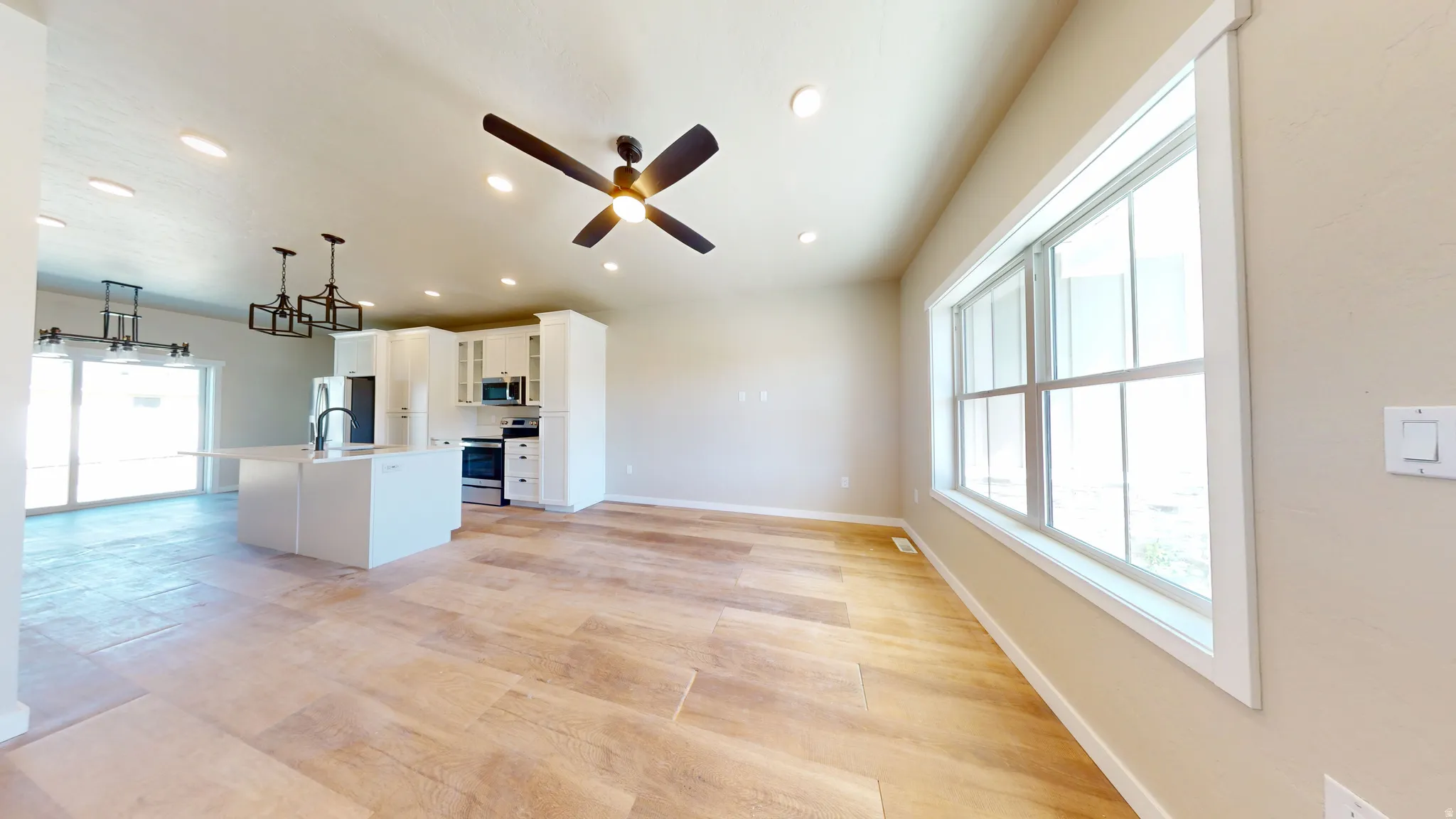 Kitchen with white cabinetry, open floor plan, a center island with sink, stainless steel appliances, and hanging light fixtures