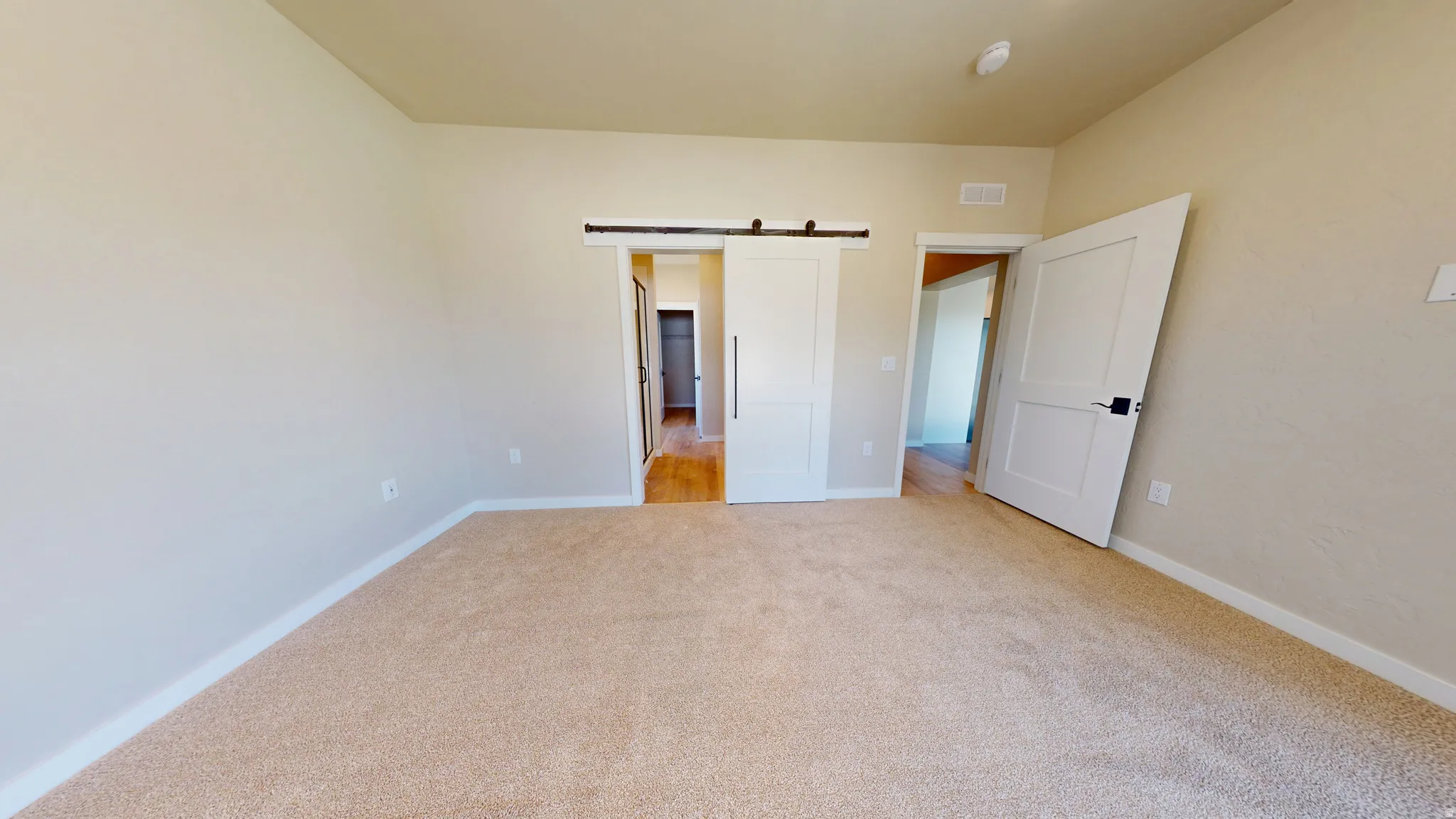 Unfurnished bedroom with a barn door and light colored carpet