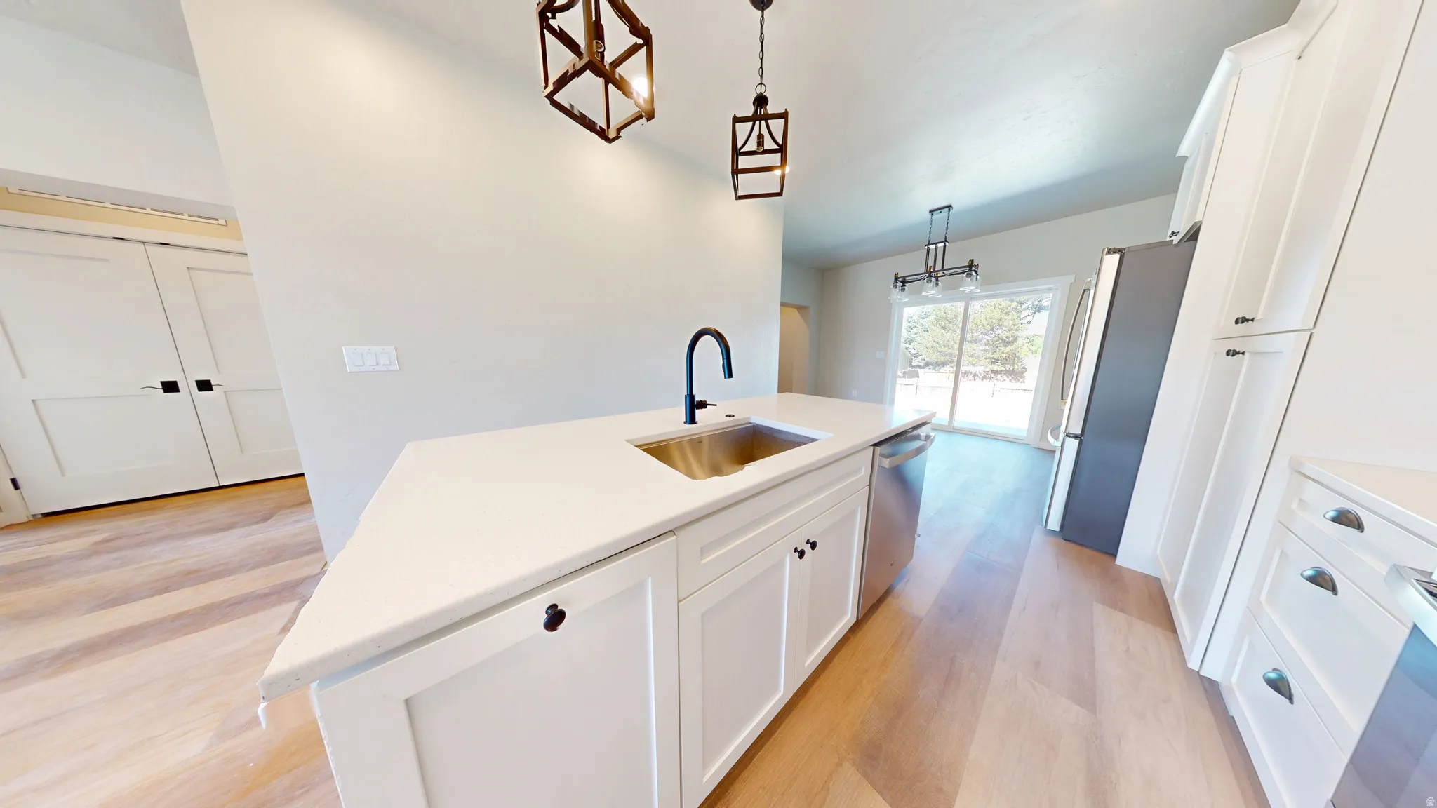 Kitchen featuring white cabinets, a center island with sink, stainless steel appliances, light wood-style flooring, and pendant lighting