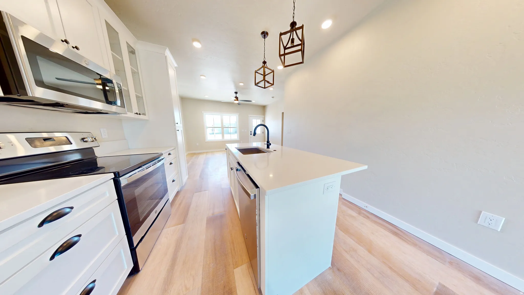 Kitchen featuring stainless steel appliances, white cabinetry, an island with sink, glass insert cabinets, and light wood-type flooring
