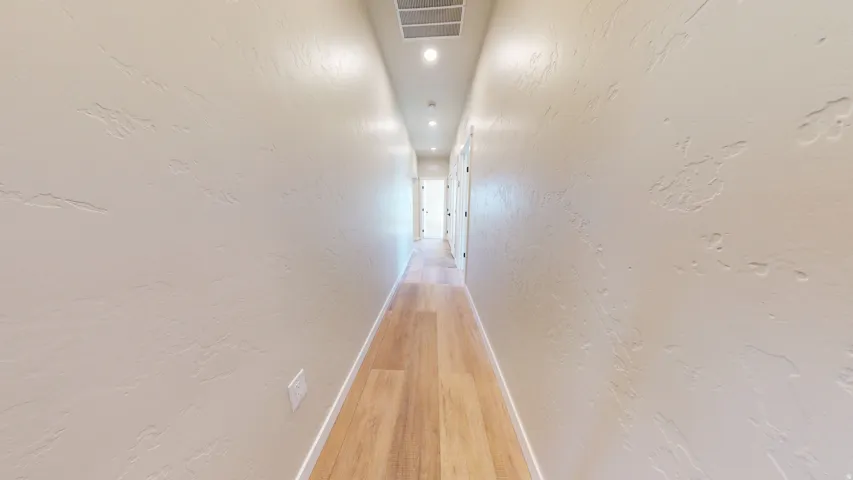 Hall featuring a textured wall, light wood-style floors, and recessed lighting