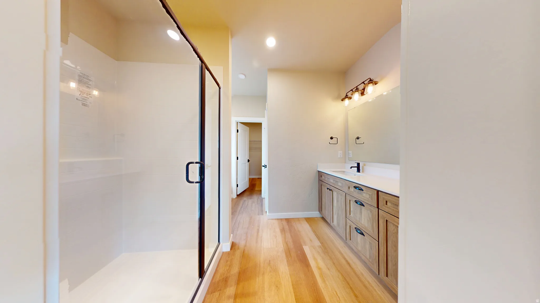 Full bathroom featuring light wood finished floors, vanity, recessed lighting, and a stall shower