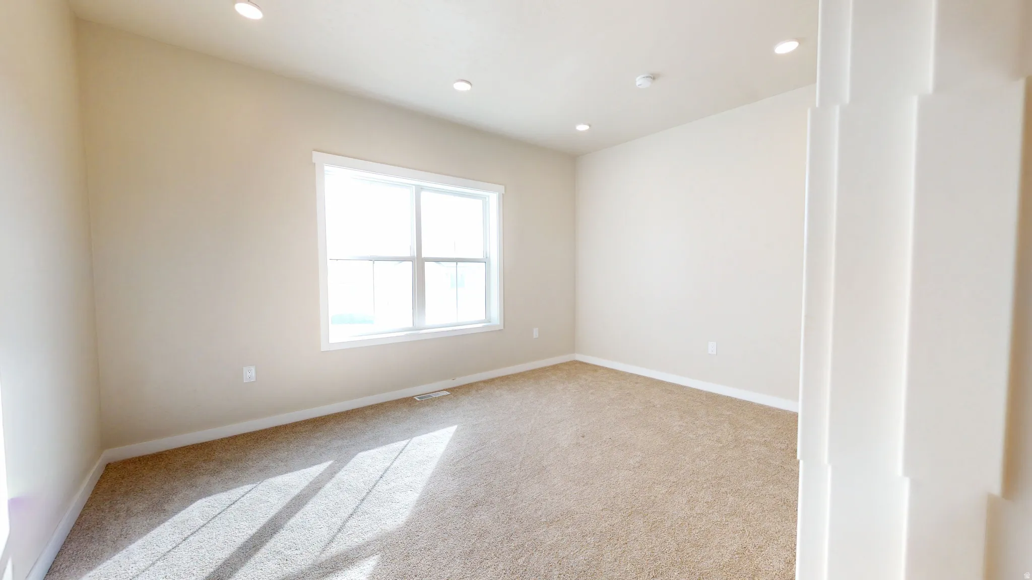 Empty room with light colored carpet and recessed lighting