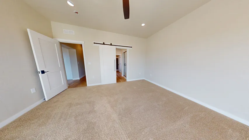 Unfurnished bedroom featuring a barn door, light carpet, recessed lighting, and a ceiling fan