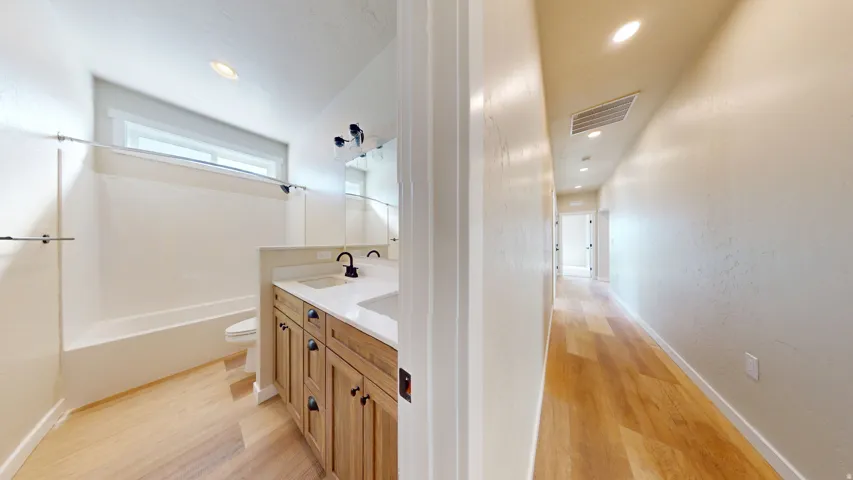 Bathroom featuring double vanity, light wood-style floors, shower / bathtub combination, and recessed lighting