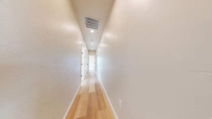 Corridor with a textured wall, light wood-type flooring, and recessed lighting