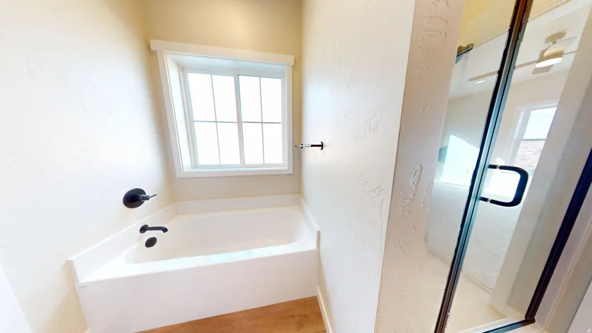 Bathroom with a textured wall, a shower stall, and a garden tub
