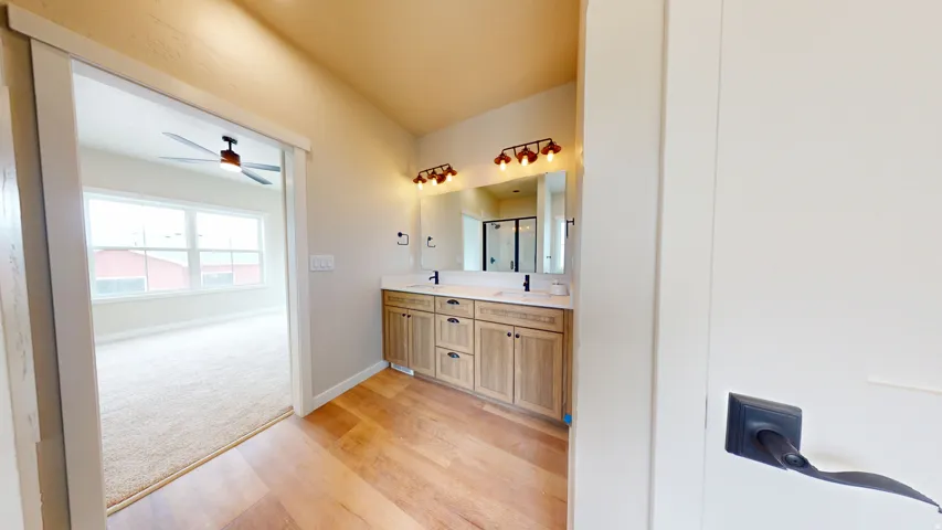 Full bath featuring double vanity, light wood-style flooring, ceiling fan, and light carpet