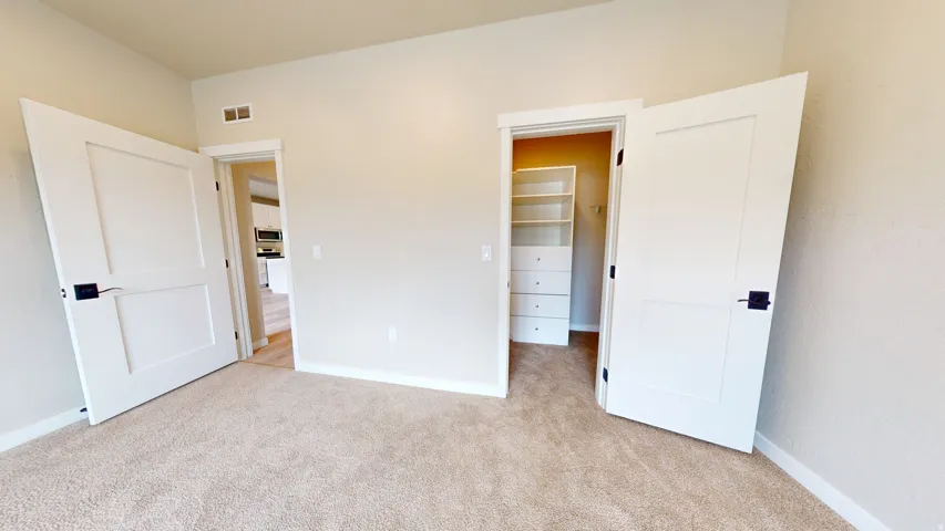 Unfurnished bedroom with a walk in closet and light carpet