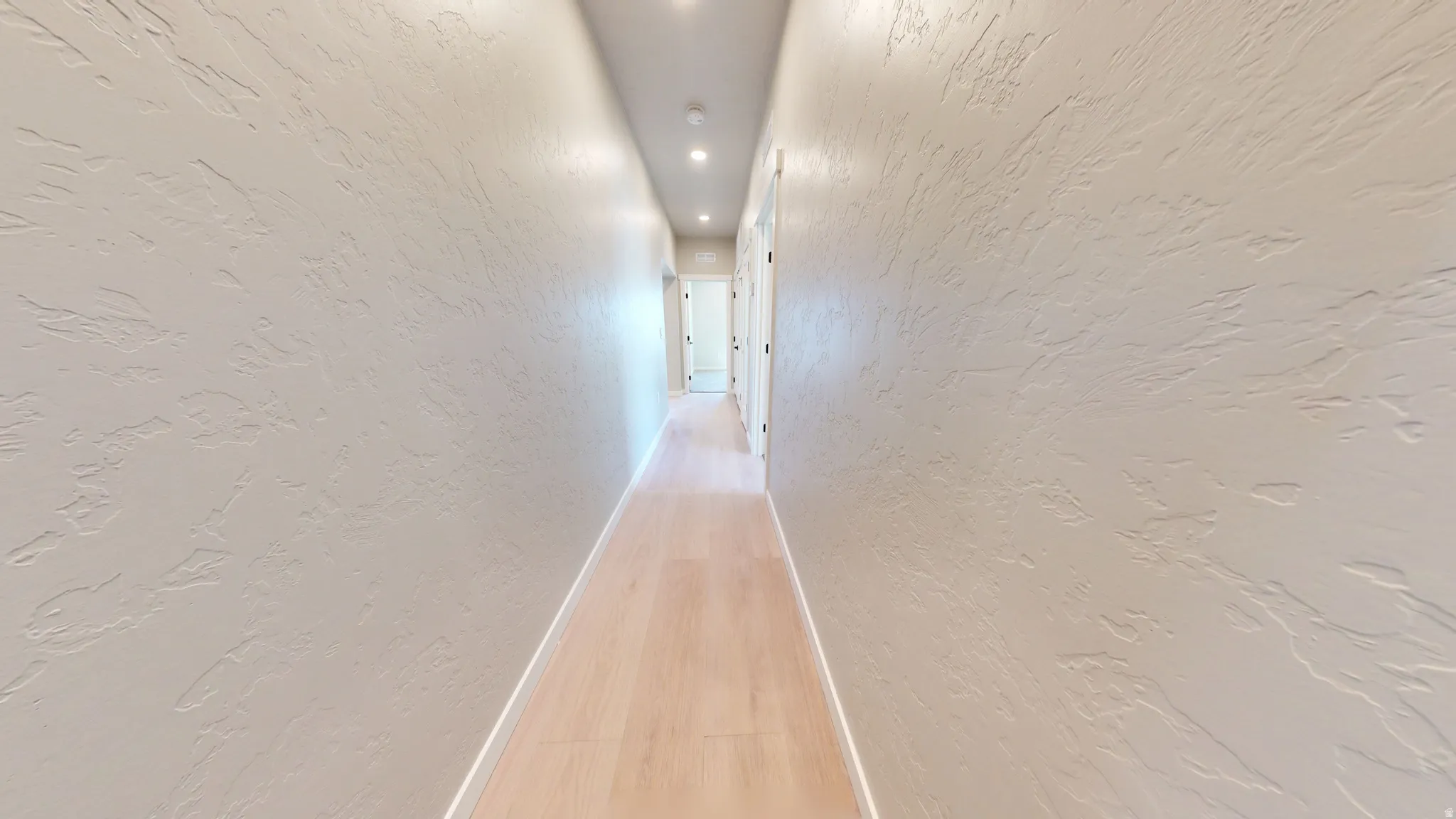 Hall featuring a textured wall, light wood-style floors, and recessed lighting