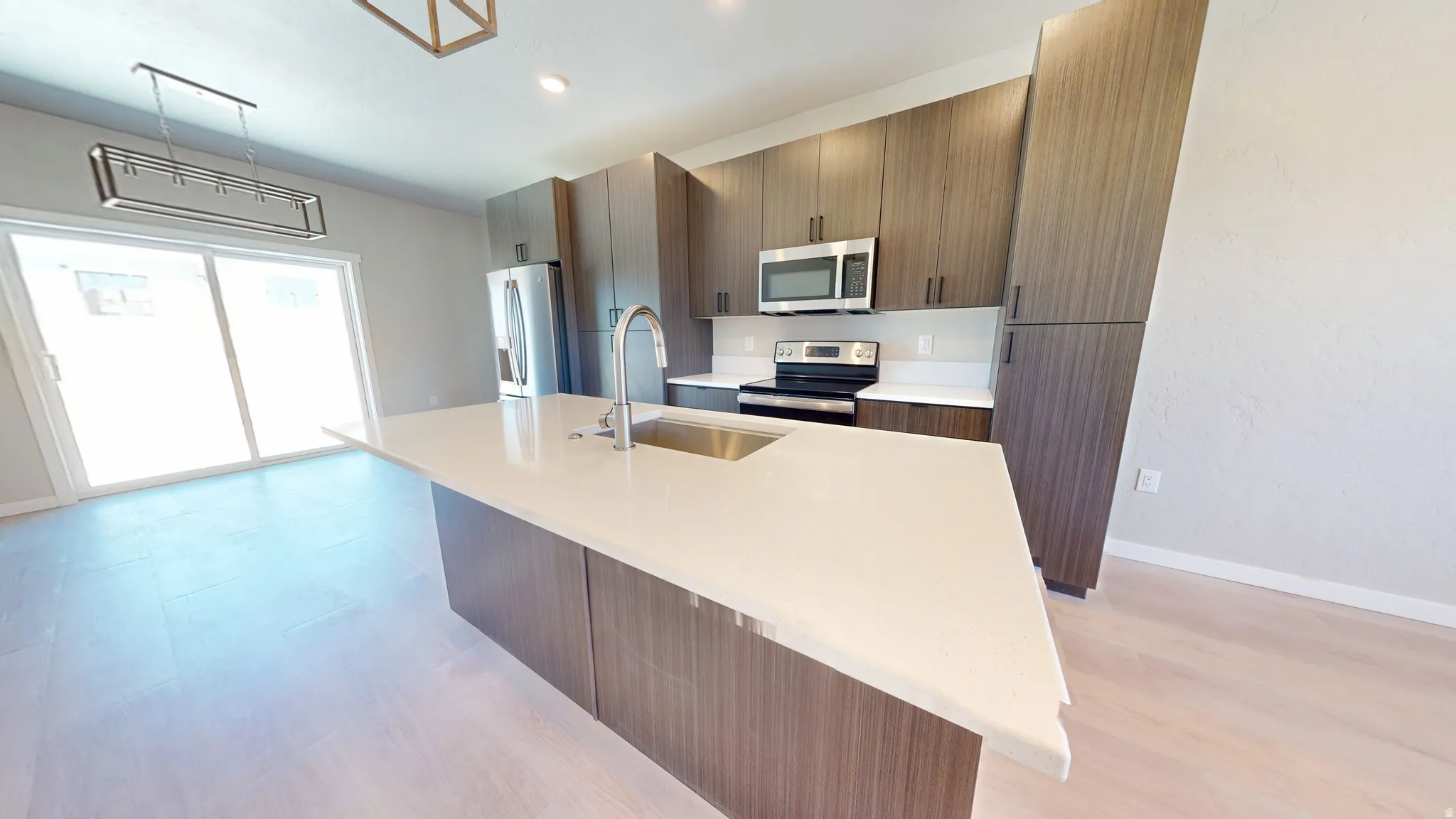 Kitchen featuring a center island with sink, appliances with stainless steel finishes, modern cabinets, light stone counters, and pendant lighting