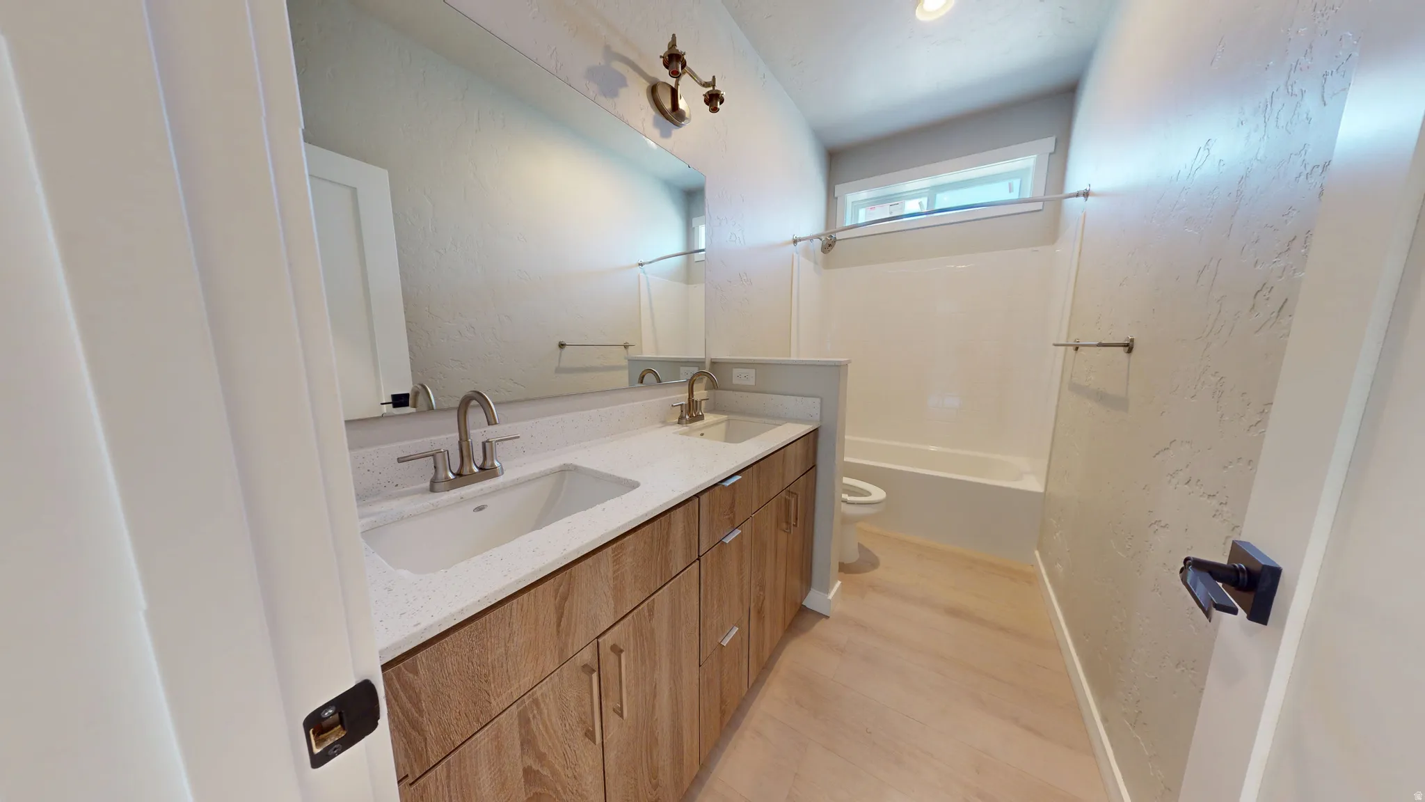 Full bath with double vanity, a textured wall, light wood-style flooring, and bathing tub / shower combination