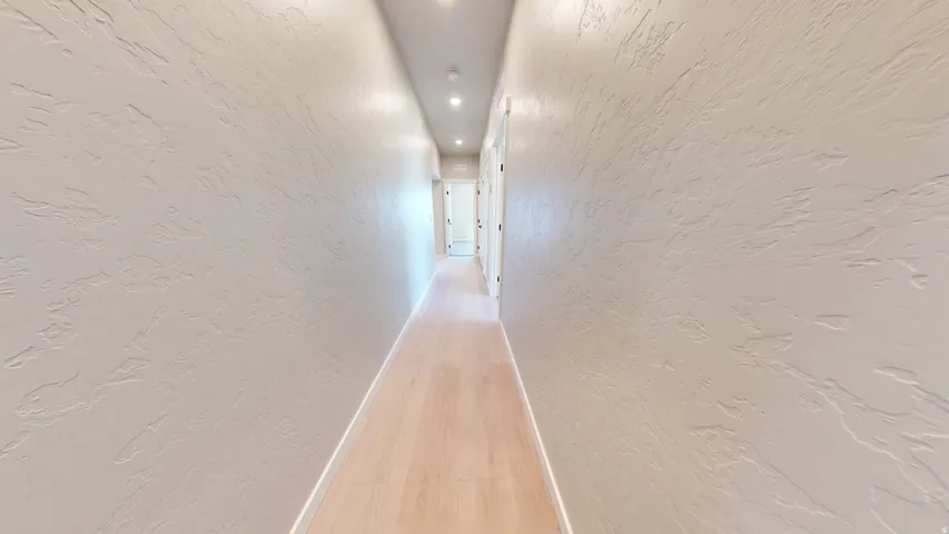 Hall featuring a textured wall, light wood-style floors, and recessed lighting