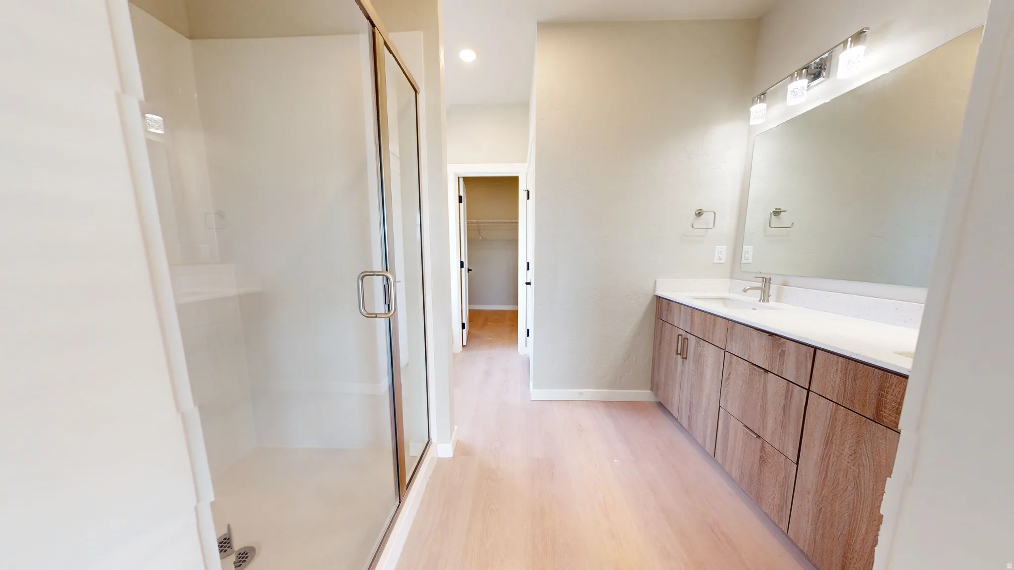 Bathroom featuring light wood-type flooring, double vanity, a shower stall, a walk in closet, and recessed lighting