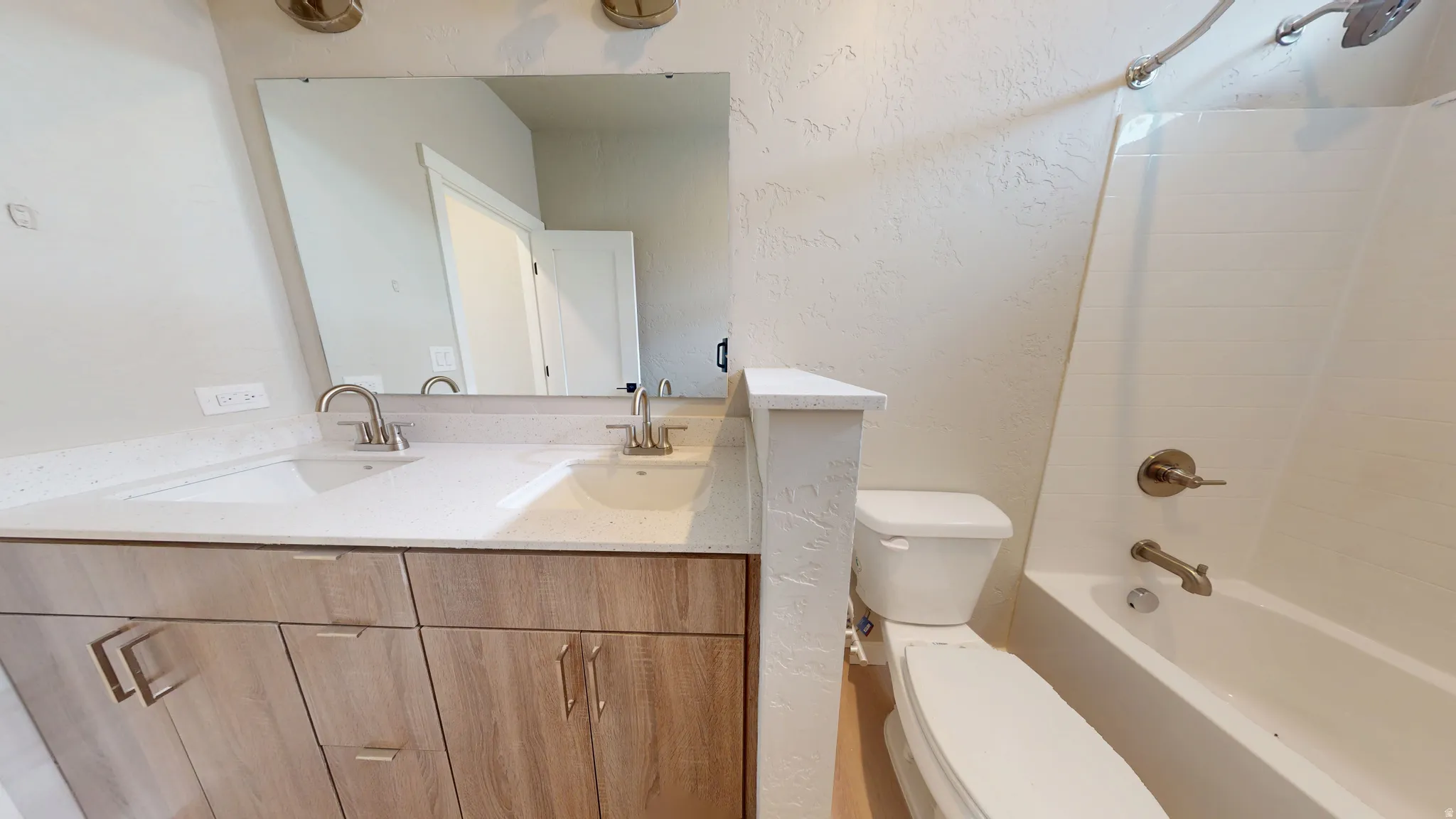 Full bath featuring a textured wall, double vanity, and bathtub / shower combination