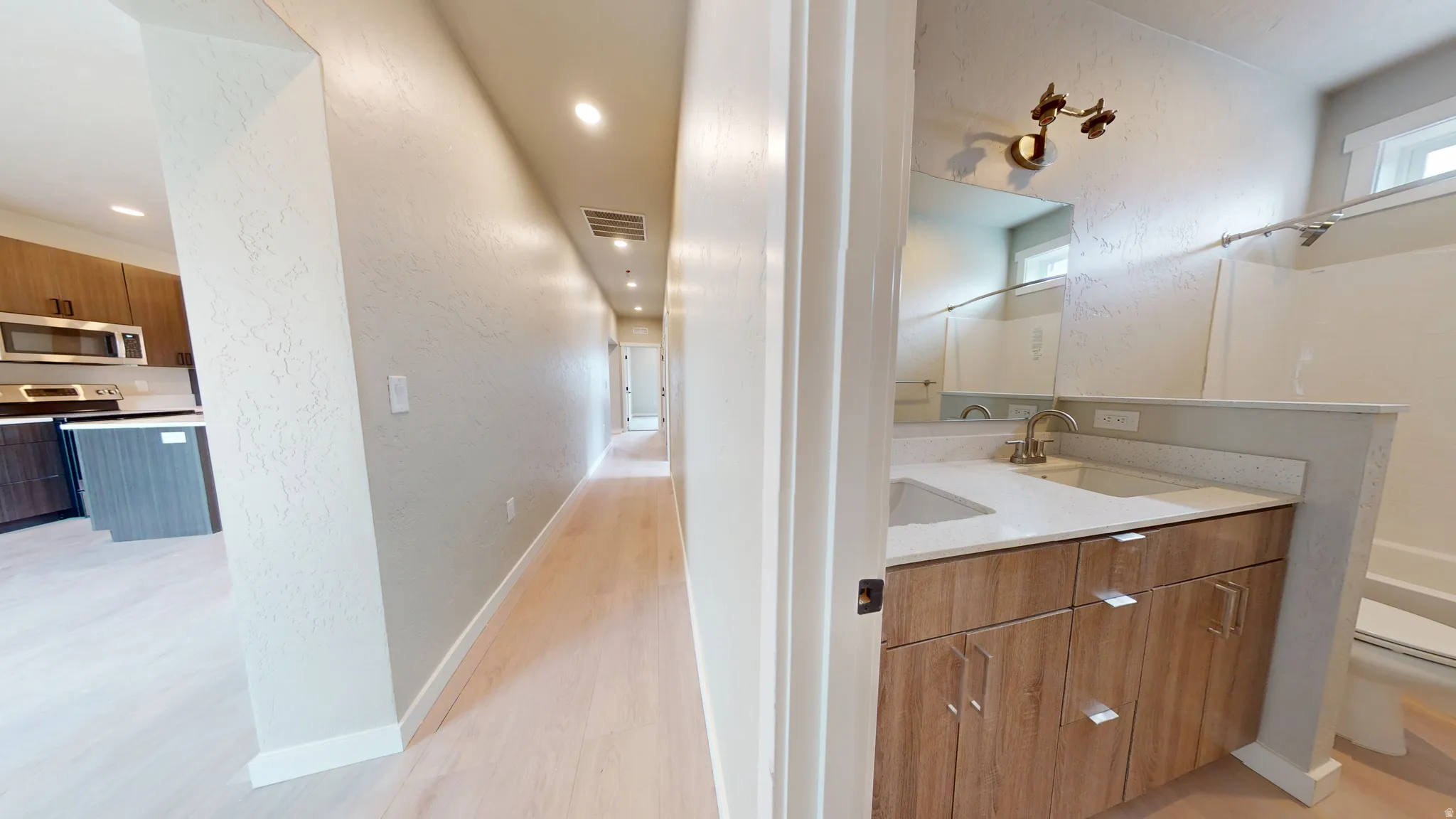 Bathroom with a textured wall, double vanity, shower / tub combination, light wood-type flooring, and recessed lighting