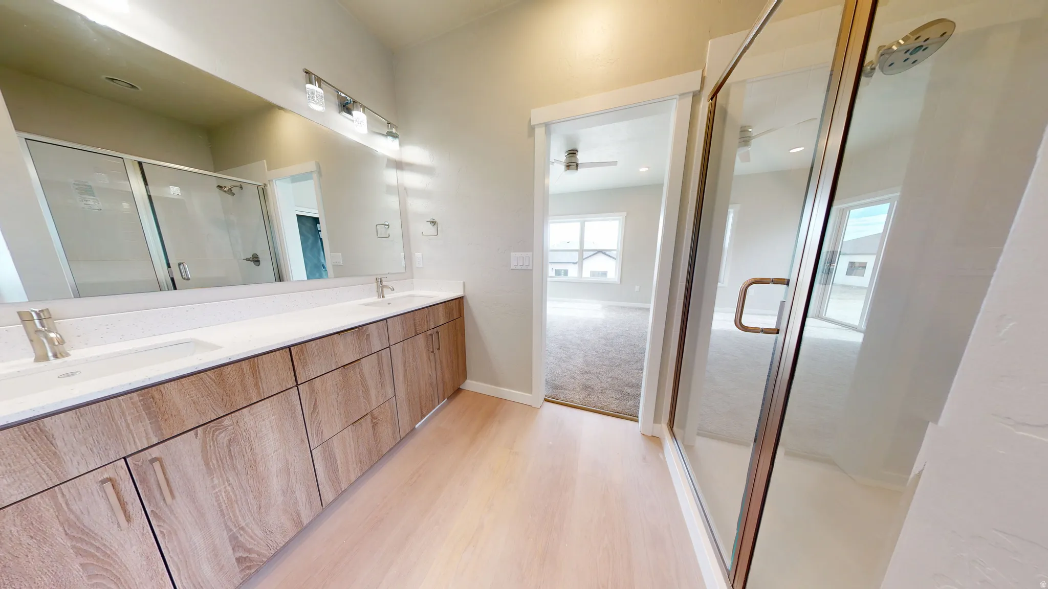 Full bathroom with a stall shower, double vanity, and light wood-style flooring
