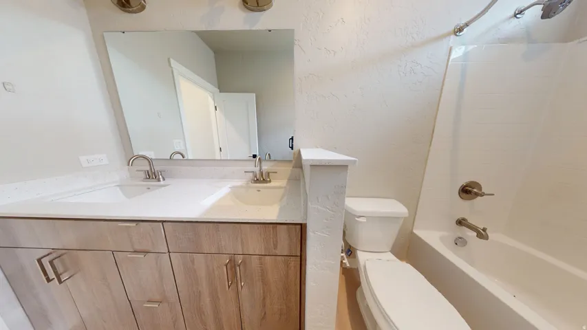 Full bath featuring a textured wall, double vanity, and bathtub / shower combination