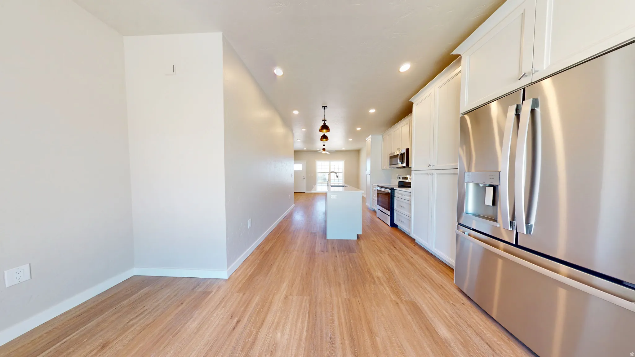 Kitchen with appliances with stainless steel finishes, white cabinets, recessed lighting, open floor plan, and light wood-style floors
