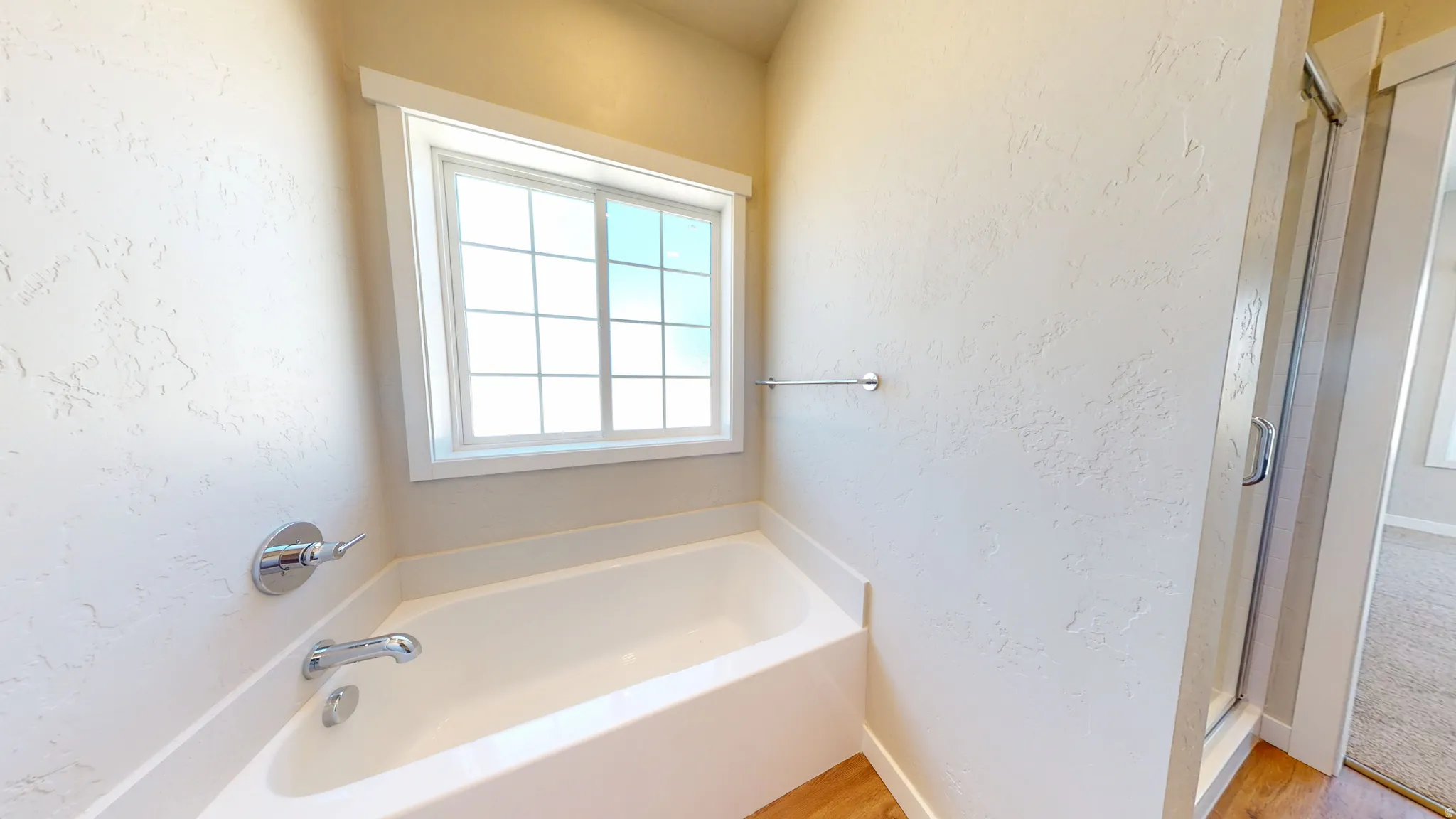 Full bathroom featuring a textured wall, a garden tub, a shower stall, and light wood finished floors