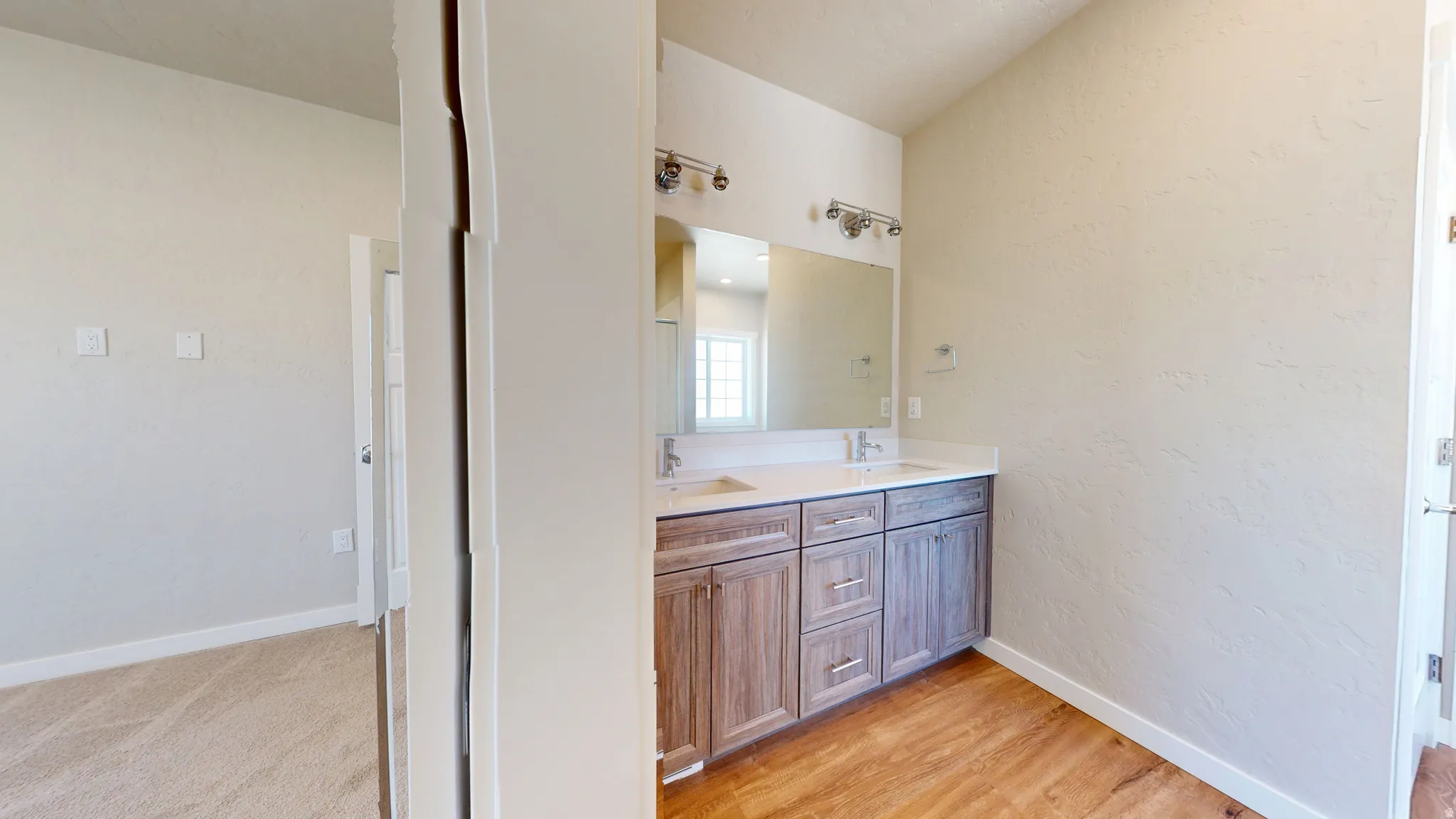 Full bath with a textured wall, double vanity, and light wood-style floors