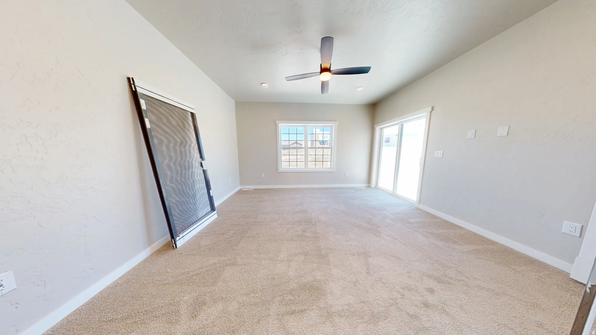 Empty room featuring light carpet, ceiling fan, and a textured wall