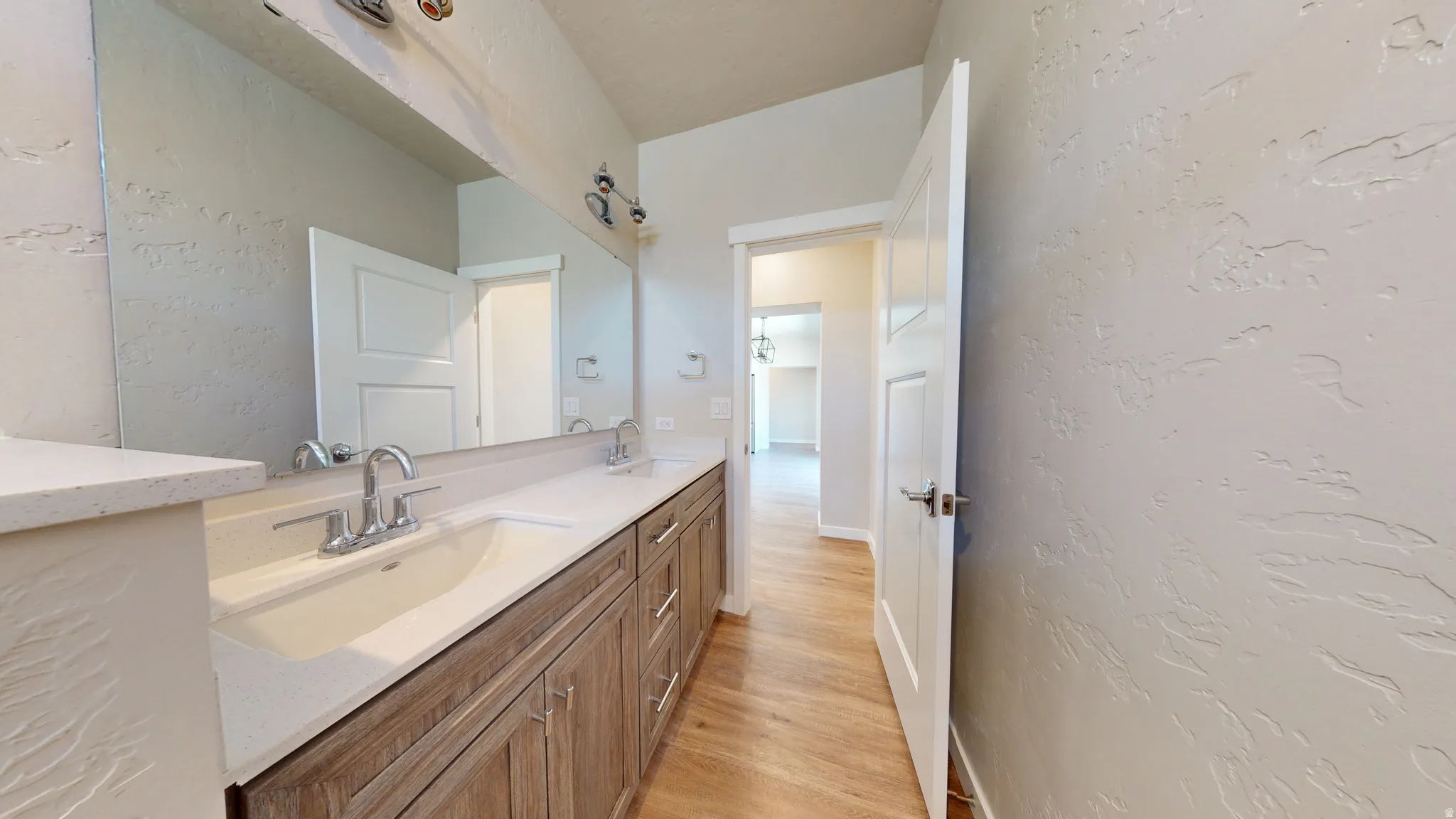 Bathroom featuring a textured wall, double vanity, and light wood finished floors