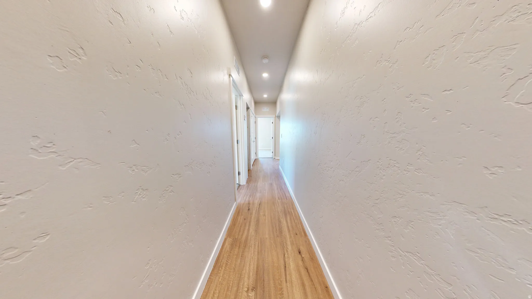 Corridor with a textured wall, recessed lighting, and light wood-type flooring