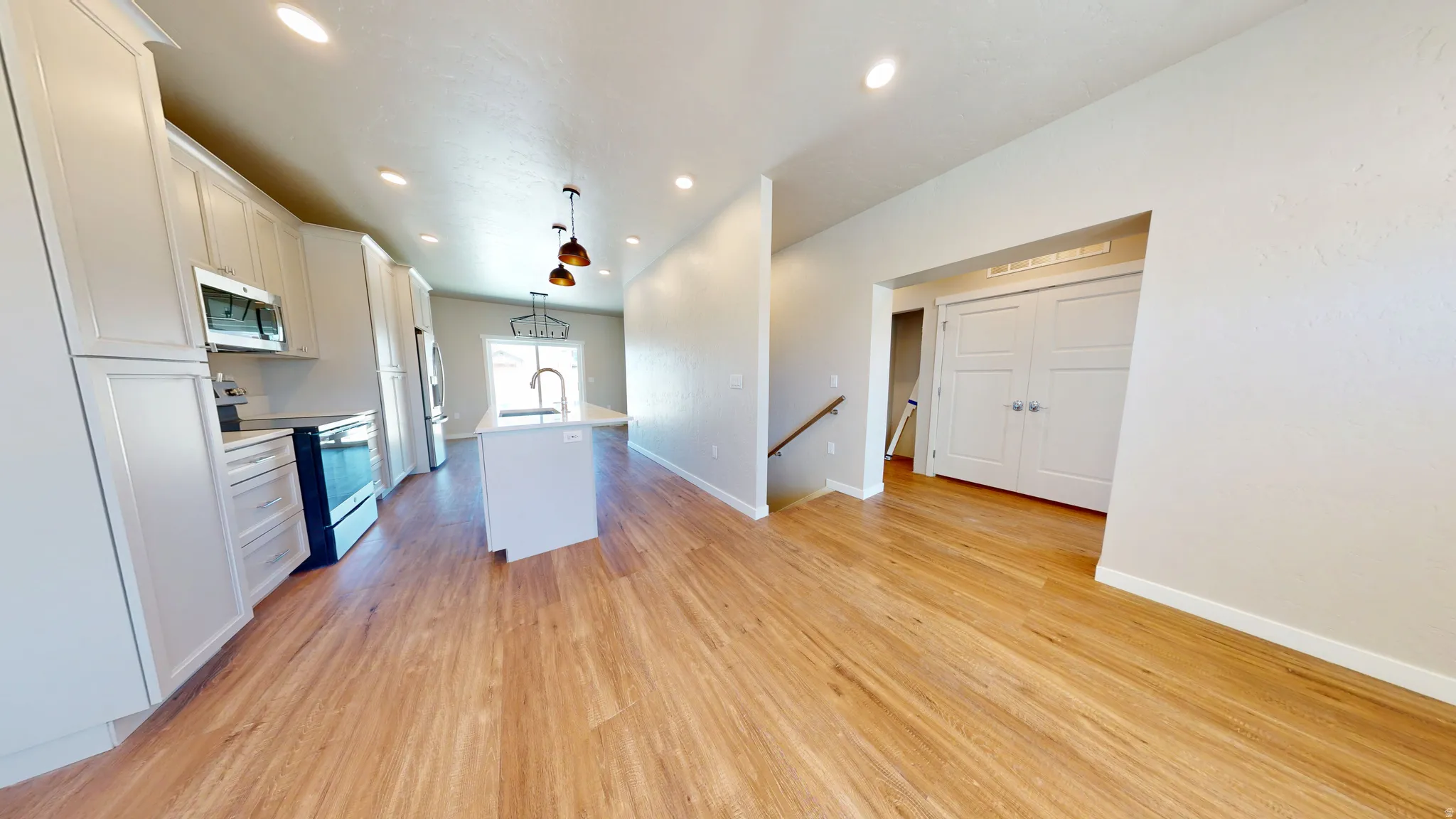 Kitchen with stainless steel appliances, hanging light fixtures, a kitchen island with sink, light wood-type flooring, and white cabinets